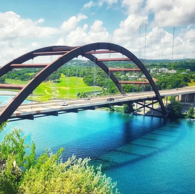 Austin Texas skyline featuring the Pennybacker Bridge over a river on a bright day