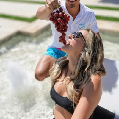 Cabana Boys host playfully popping champagne near a laughing female guest in a pool