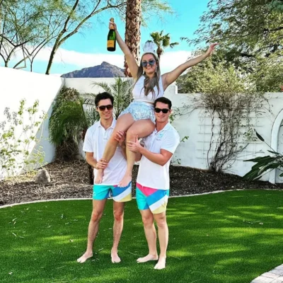 Two Cabana Boys hosts in white shirts and colorful swim trunks posing on a lush lawn