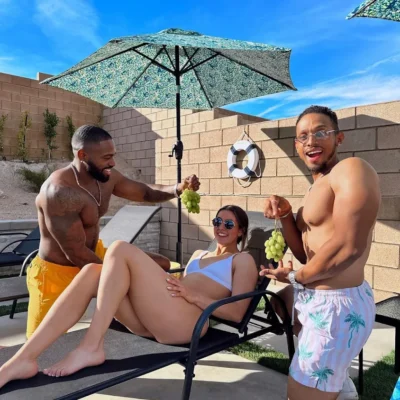 Two shirtless Cabana Boys hosts posing with female guests under a patio umbrella poolside