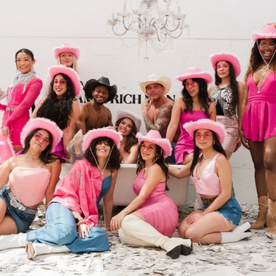 A large bachelorette group in pink bunny ears and cowboy hats posing with a Cocktail Cowboys host indoors