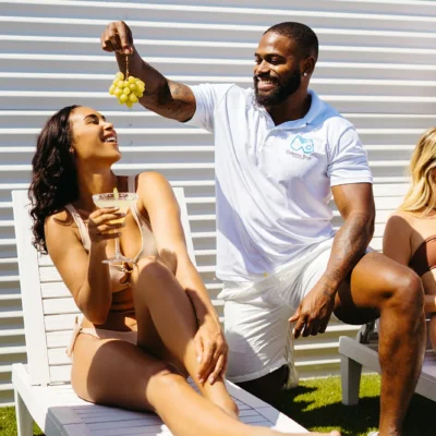 Cabana Boys host in white polo sharing a moment and drinks with a female guest poolside
