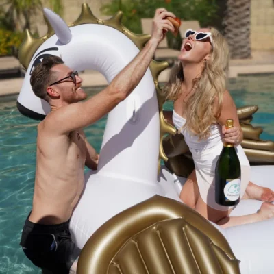 A Cabana Boys host reclining on a gold inflatable while holding a champagne bottle at a pool party