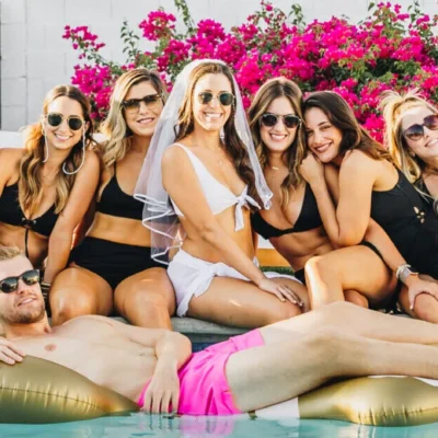 Group of women in swimwear lounging together outdoors surrounded by pink floral backdrop