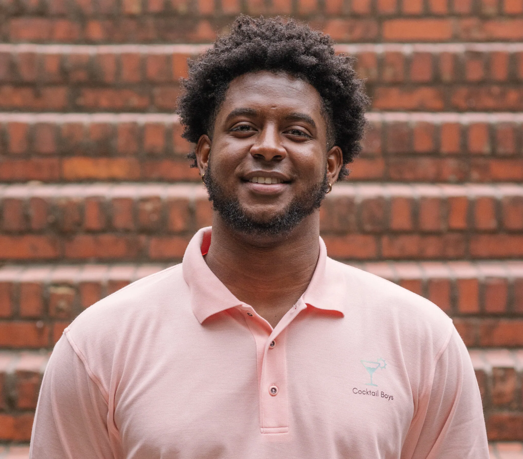 Headshot of a smiling Cabana Boys host in a pink polo against a red brick wall
