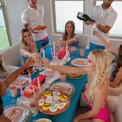 A Cabana Boys host serving a colorful spread of food and drinks to women at an outdoor party table