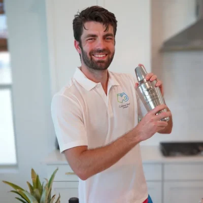 A smiling Cabana Boys host in a white polo holding a bottle at an outdoor party