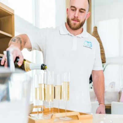 A Cabana Boys host pouring champagne into glasses on a tray in a bright modern kitchen
