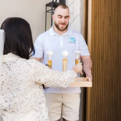 A Cabana Boys host in a white polo presenting a tray of champagne flutes to a woman indoors