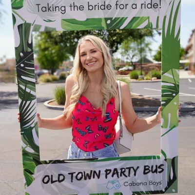 A woman in a floral top posing with an Old Town Party Bus sign with a Cabana Boys host