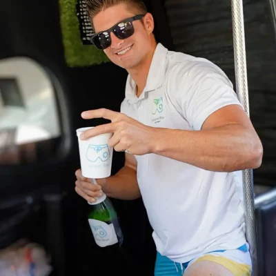 A Cabana Boys host in a white polo holding a cup and giving a thumbs up inside a party bus