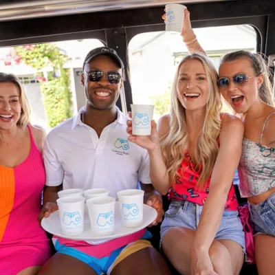A Cabana Boys host and two women in bright swimsuits posing outside a party bus