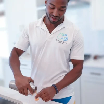 A Cabana Boys host in a white polo preparing drinks at a poolside bar table