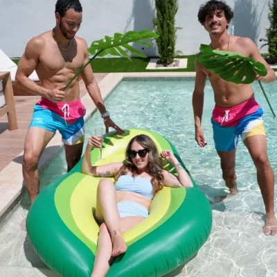 A Cabana Boys host in colorful shorts jumping onto an avocado pool float in a backyard pool