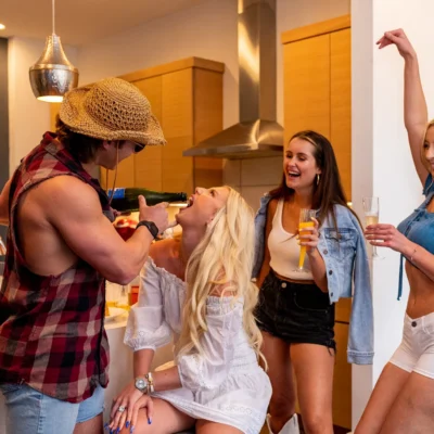 A Cocktail Cowboys host in plaid playfully dancing with a laughing woman in a white dress indoors