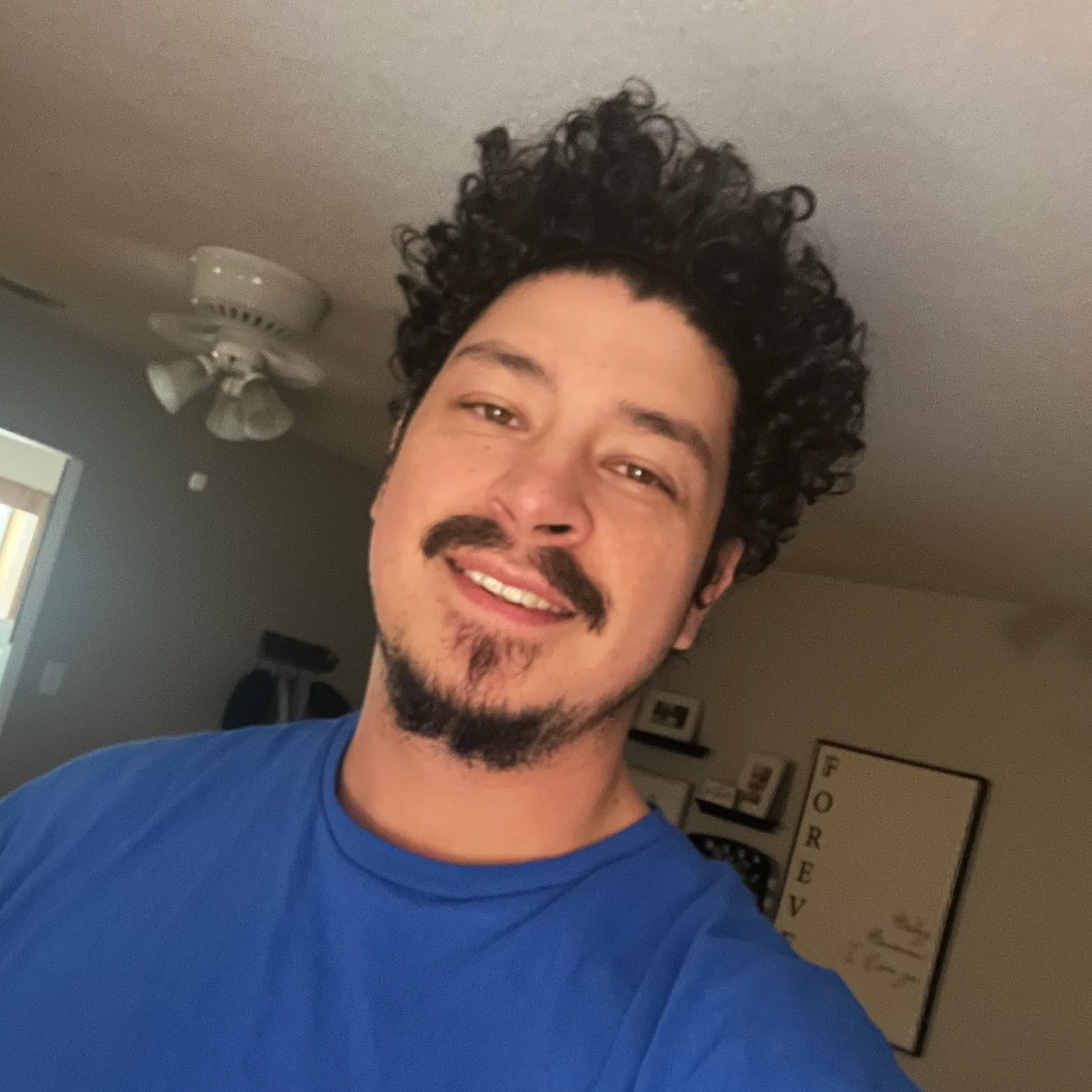 Headshot of a smiling Cabana Boys host with curly hair in a blue shirt indoors