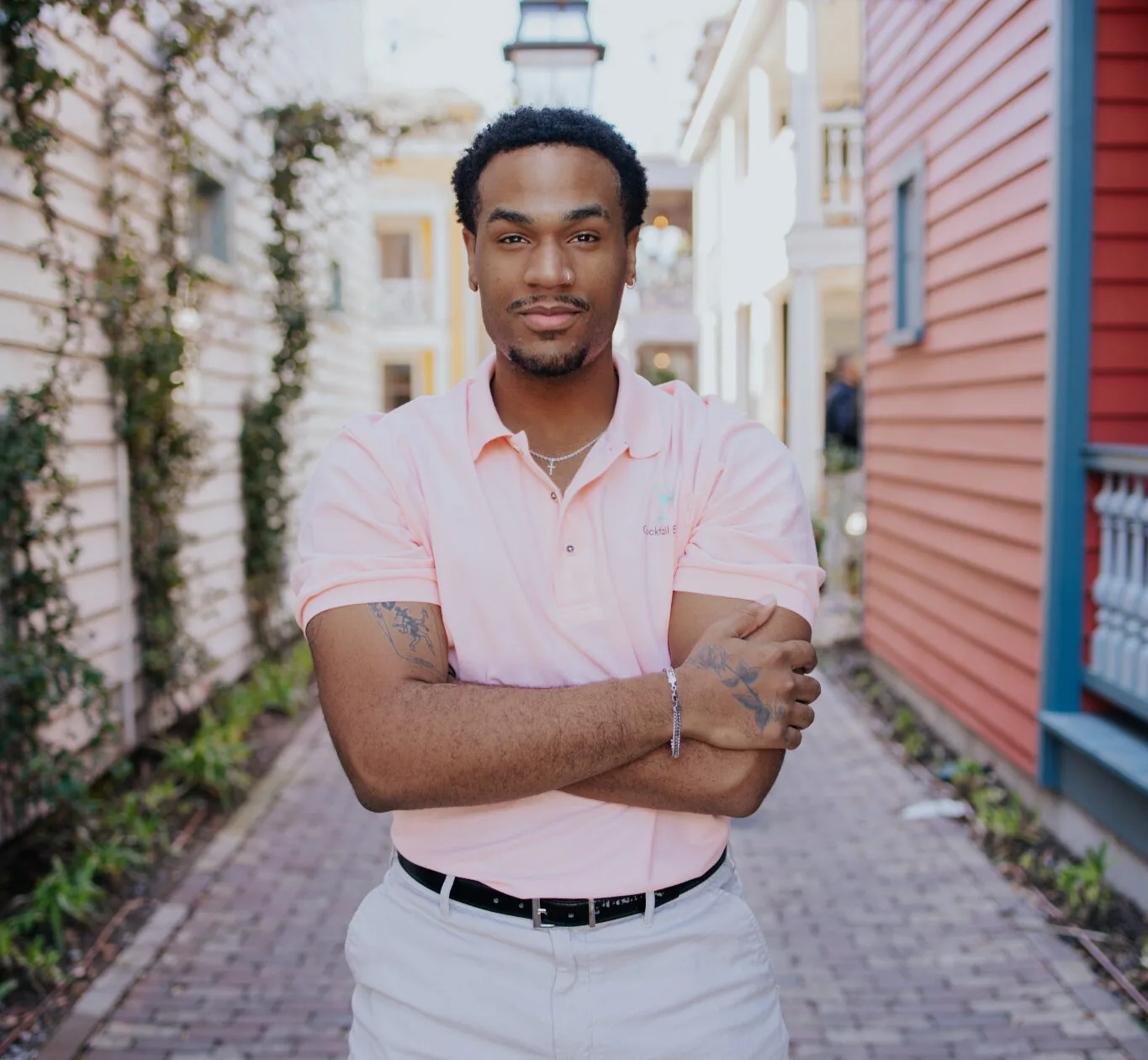 A Cabana Boys host in a white polo standing with arms crossed in a charming ivy-covered Charleston alleyway