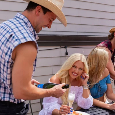 A Cocktail Cowboys host in plaid leaning in to serve food to a smiling blonde woman indoors