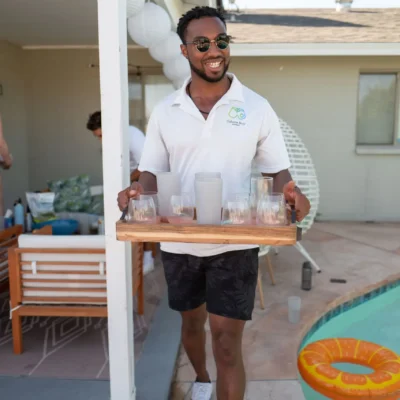 Cabana Boys host in white polo setting up a drink station at an outdoor pool event