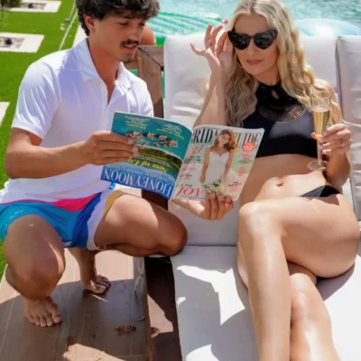 A Cabana Boys host reading a menu or magazine to a woman in sunglasses relaxing at a pool party