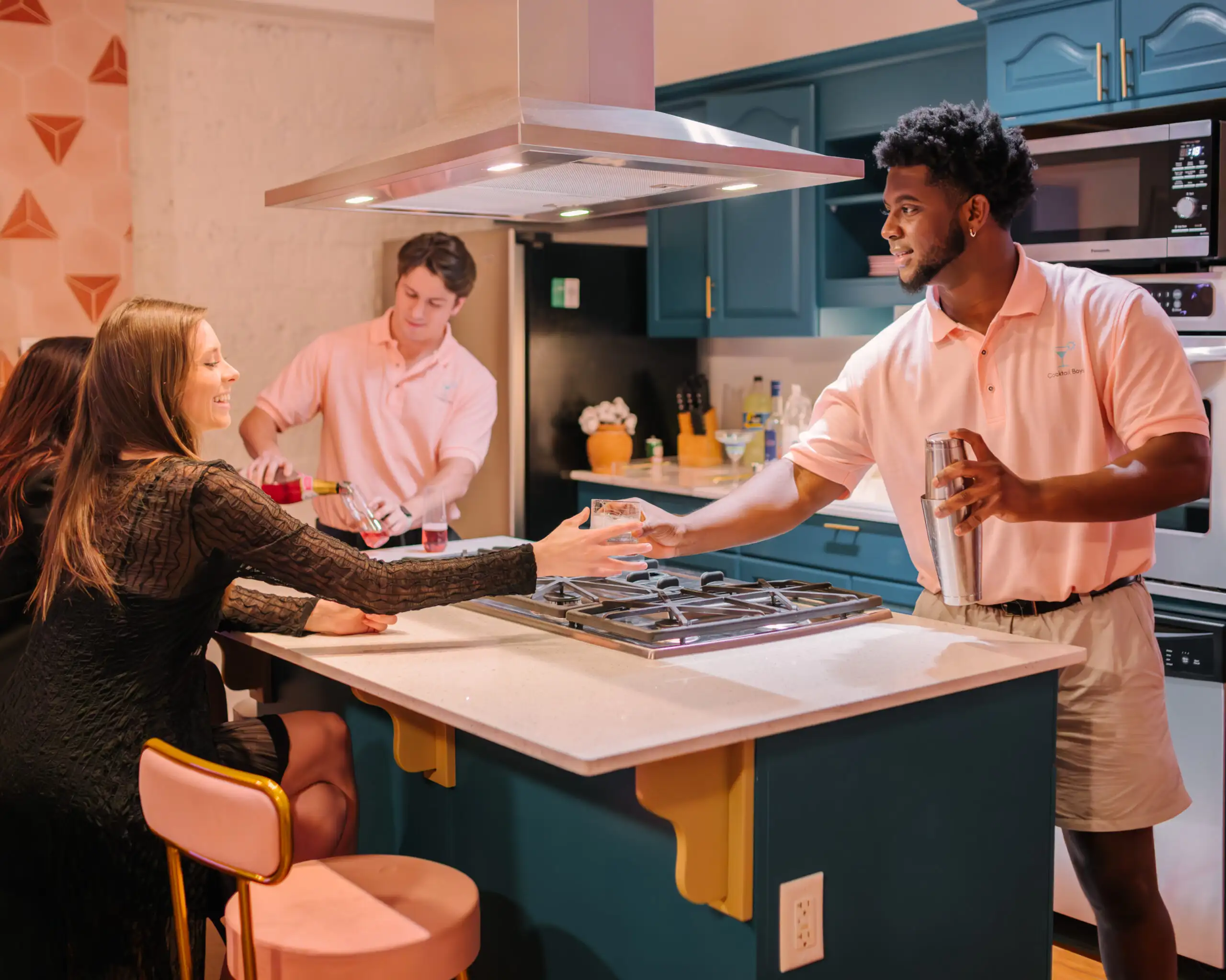 Two Cocktail Boys hosts in pink shirts working together in a modern teal-accented kitchen