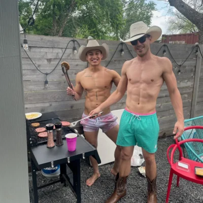Two shirtless Cocktail Cowboys hosts in cowboy hats grilling food at an outdoor backyard party
