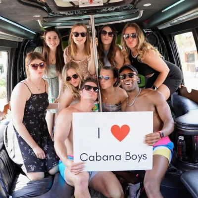 A large group holding an "I Love Cabana Boys" sign inside a decorated party bus